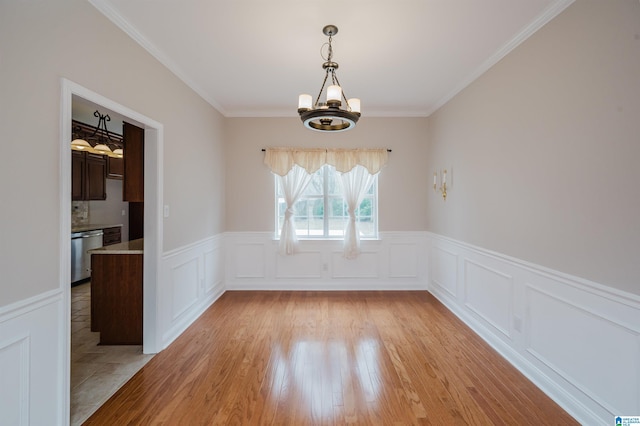 unfurnished dining area featuring a chandelier, wainscoting, light wood-type flooring, and crown molding