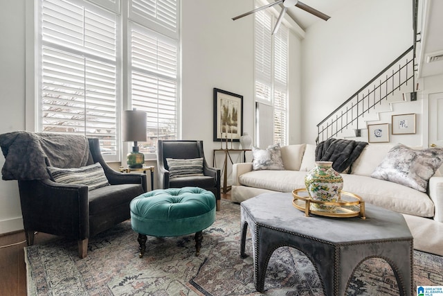 living area with a ceiling fan, stairway, a high ceiling, and wood finished floors