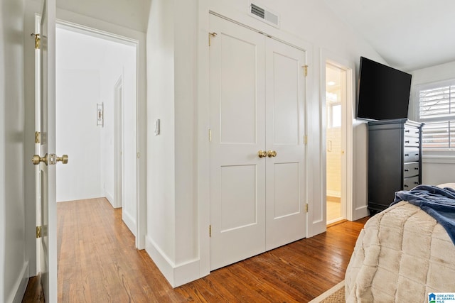 bedroom with lofted ceiling, light wood-style flooring, visible vents, baseboards, and ensuite bath