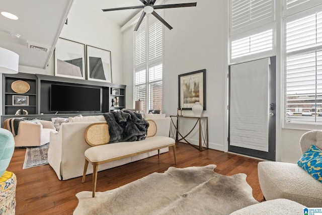 living room featuring a ceiling fan, a towering ceiling, visible vents, baseboards, and dark wood finished floors