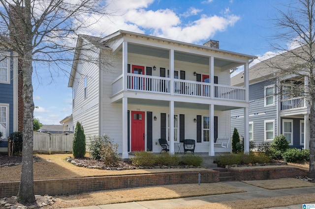 view of front of home featuring a porch, a chimney, fence, and a balcony