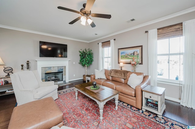 living room featuring dark wood-style floors, plenty of natural light, ornamental molding, and a tiled fireplace