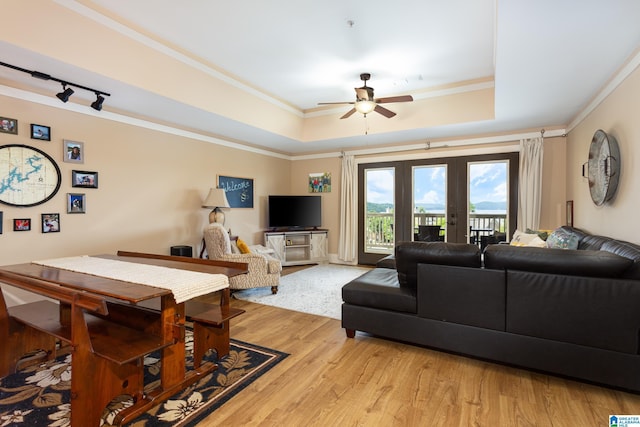 living area featuring a tray ceiling, french doors, light wood-style flooring, ornamental molding, and a ceiling fan