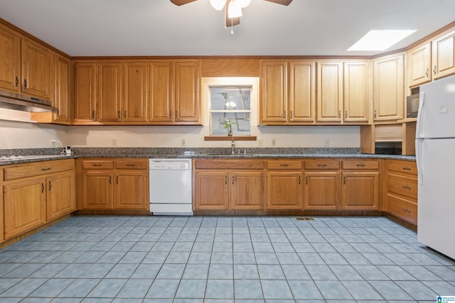 kitchen featuring white appliances, a skylight, brown cabinetry, under cabinet range hood, and a sink