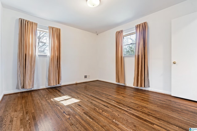 spare room with a healthy amount of sunlight, visible vents, baseboards, and wood finished floors