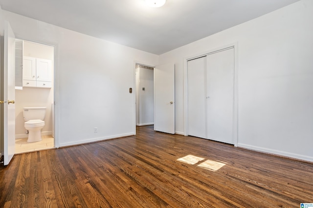 unfurnished bedroom featuring dark wood-type flooring, a closet, ensuite bath, and baseboards