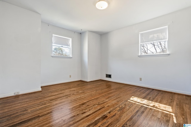 empty room featuring wood finished floors, visible vents, and baseboards