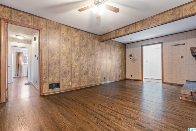 unfurnished living room with visible vents, attic access, dark wood-type flooring, ceiling fan, and baseboards