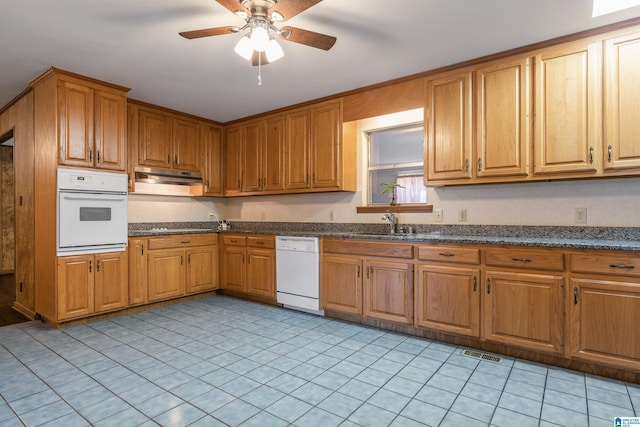 kitchen featuring under cabinet range hood, white appliances, visible vents, brown cabinetry, and dark countertops