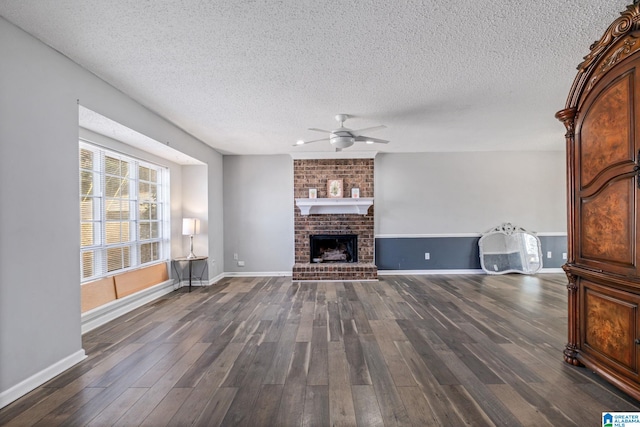 unfurnished living room with a fireplace, dark wood finished floors, a ceiling fan, a textured ceiling, and baseboards