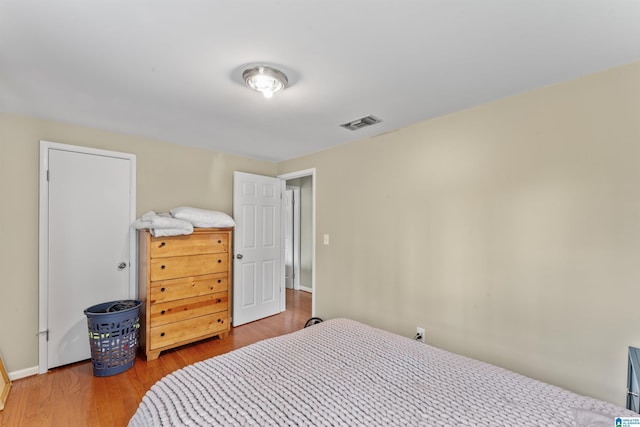 bedroom with baseboards, visible vents, and wood finished floors