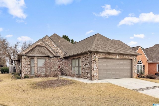 french country style house with a shingled roof, concrete driveway, brick siding, and a front lawn