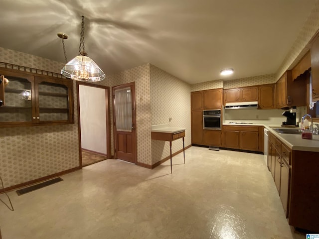 kitchen featuring oven, under cabinet range hood, a sink, visible vents, and wallpapered walls