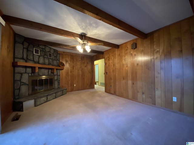 unfurnished living room with ceiling fan, a stone fireplace, wood walls, visible vents, and beam ceiling