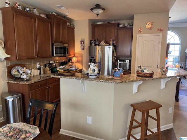 kitchen with light stone counters, a center island, stainless steel appliances, decorative backsplash, and a kitchen bar