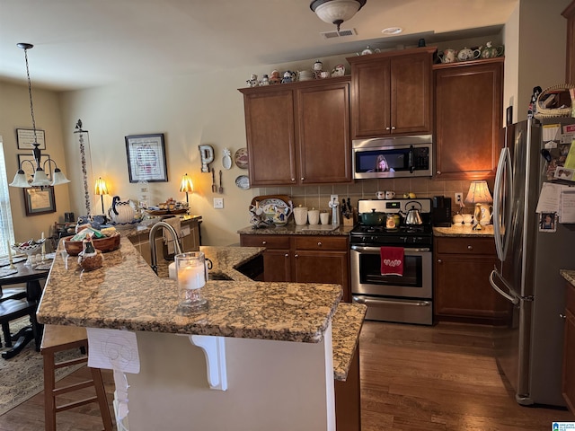 kitchen with light stone counters, stainless steel appliances, a breakfast bar, a center island with sink, and pendant lighting