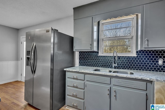 kitchen with gray cabinetry, wainscoting, a sink, and stainless steel fridge with ice dispenser