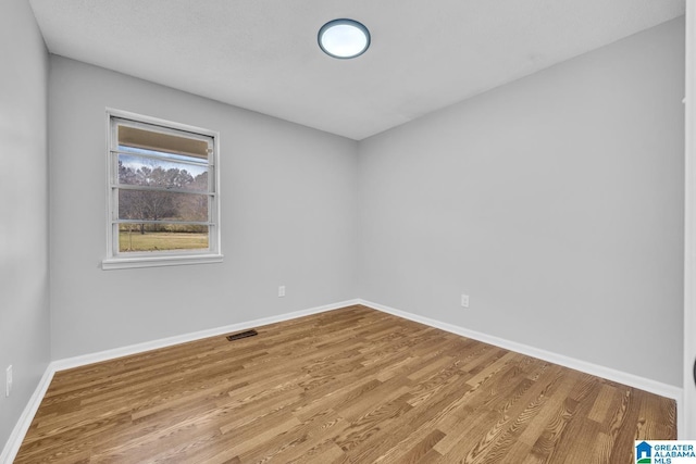 spare room with light wood-type flooring, visible vents, and baseboards