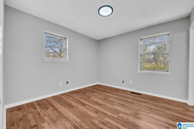 spare room featuring wood finished floors, visible vents, and baseboards