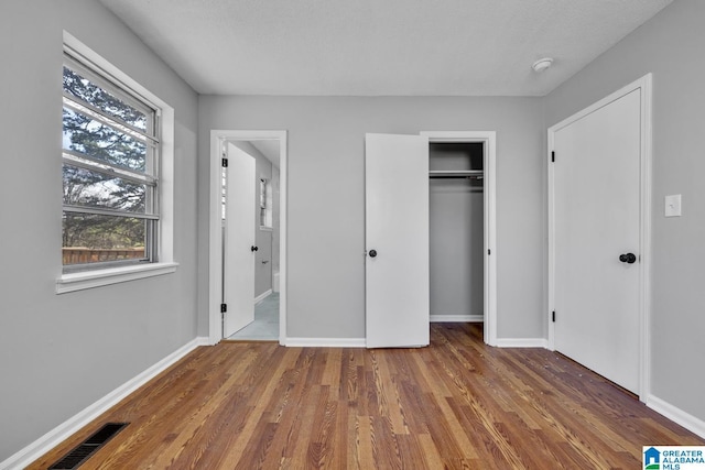 unfurnished bedroom featuring a closet, dark wood-style flooring, visible vents, and baseboards