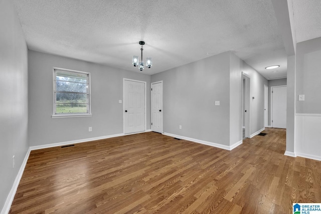 interior space featuring a textured ceiling, baseboards, wood finished floors, and a notable chandelier