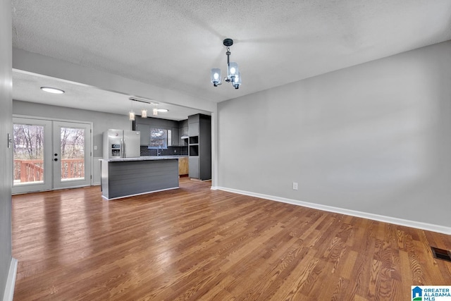 unfurnished living room with baseboards, french doors, dark wood-type flooring, and a notable chandelier