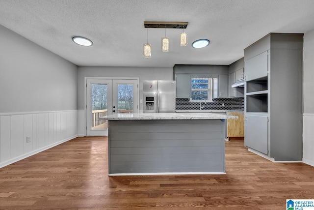 kitchen with light stone counters, decorative light fixtures, stainless steel refrigerator with ice dispenser, gray cabinetry, and a kitchen island