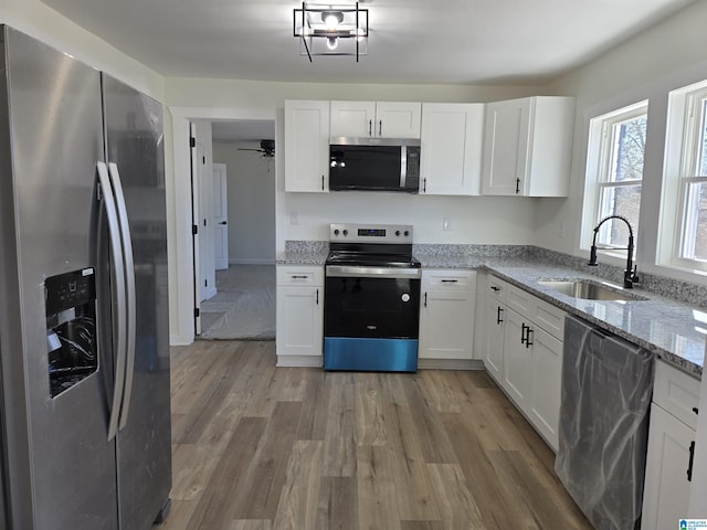 kitchen with light stone countertops, white cabinetry, stainless steel appliances, and a sink