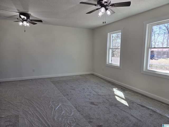 empty room featuring a ceiling fan, dark colored carpet, a textured ceiling, and baseboards