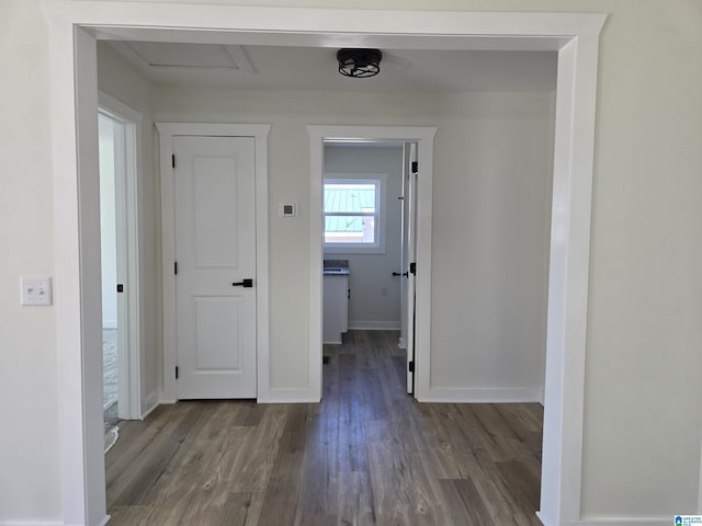 hallway featuring attic access, dark wood-style flooring, and baseboards