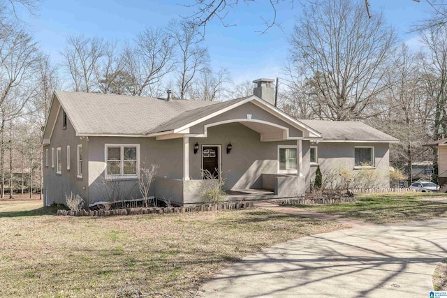 view of front of home with roof with shingles, a chimney, a front lawn, and stucco siding