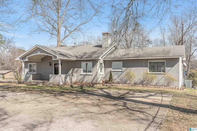 ranch-style home featuring a chimney, covered porch, central AC unit, and stucco siding