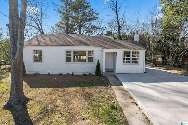 single story home featuring concrete block siding, roof with shingles, and a chimney