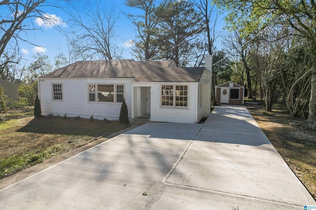 view of front of property with concrete driveway, a chimney, concrete block siding, roof with shingles, and an outbuilding