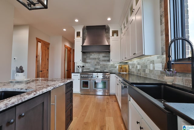 kitchen featuring stainless steel appliances, a sink, white cabinets, custom exhaust hood, and glass insert cabinets