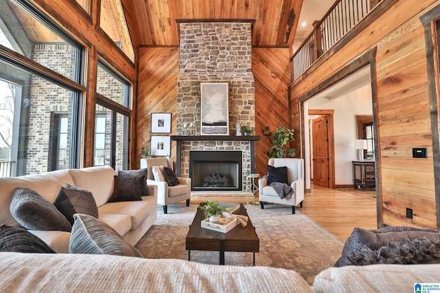 living area featuring light wood-style floors, wooden walls, a high ceiling, and a stone fireplace