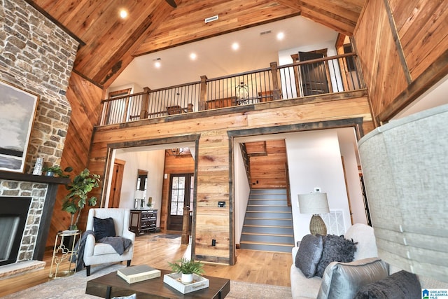 living area featuring wood ceiling, light wood-style flooring, stairway, a stone fireplace, and high vaulted ceiling