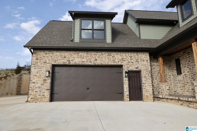 exterior space featuring a garage, concrete driveway, roof with shingles, and stone siding