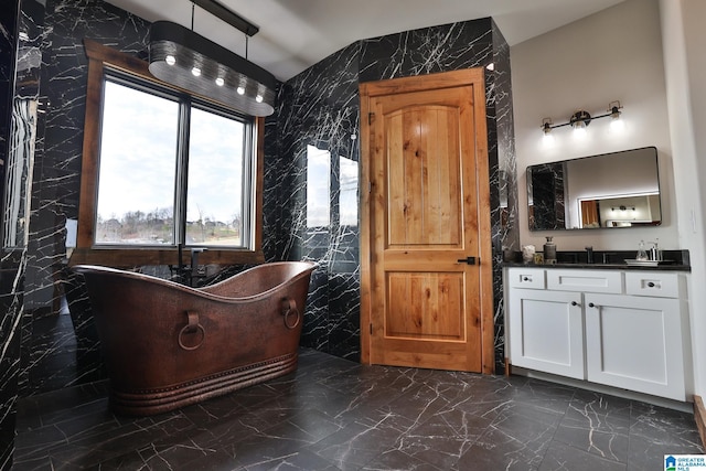 full bath featuring tile walls, a freestanding tub, marble finish floor, and vanity