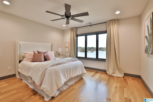 bedroom featuring a water view, light wood finished floors, and baseboards