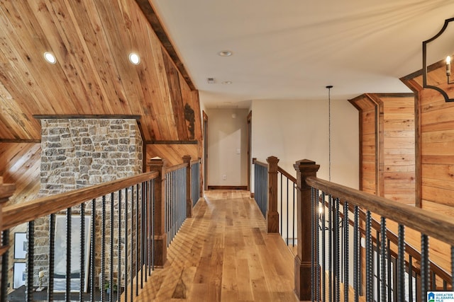 hall featuring light wood-style floors, recessed lighting, an upstairs landing, and wooden walls