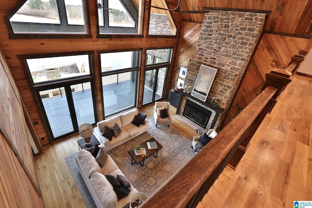 living area featuring light wood-style flooring, wood walls, a stone fireplace, and high vaulted ceiling