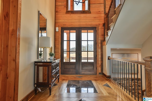 foyer featuring baseboards, wooden walls, stairway, and french doors