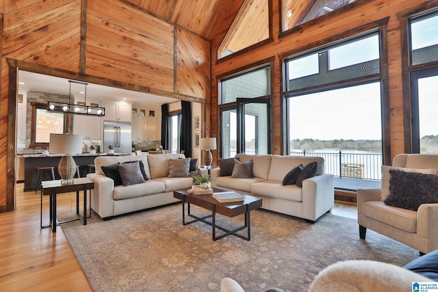 living room with high vaulted ceiling, wooden ceiling, wood walls, a water view, and light wood finished floors