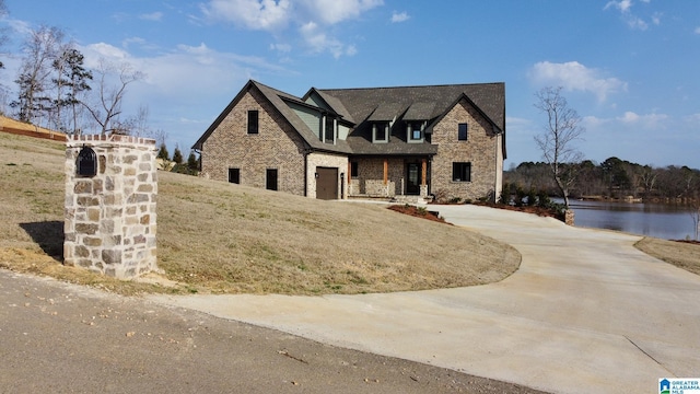 view of front of property featuring stone siding, concrete driveway, and a water view