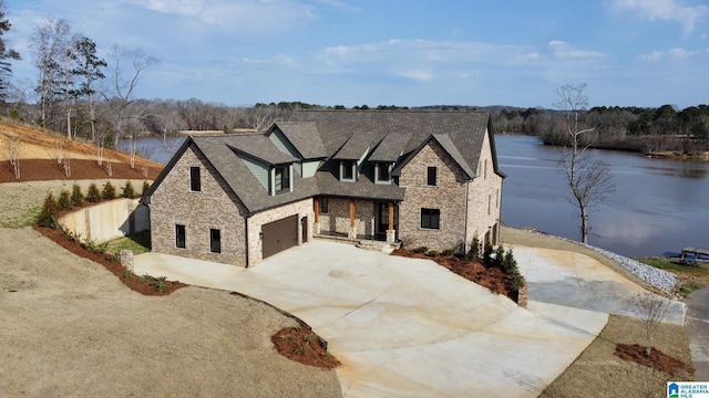 view of front of property featuring stone siding, a water view, an attached garage, and concrete driveway