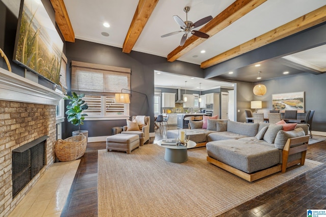 living area featuring a brick fireplace, beamed ceiling, baseboards, and wood finished floors