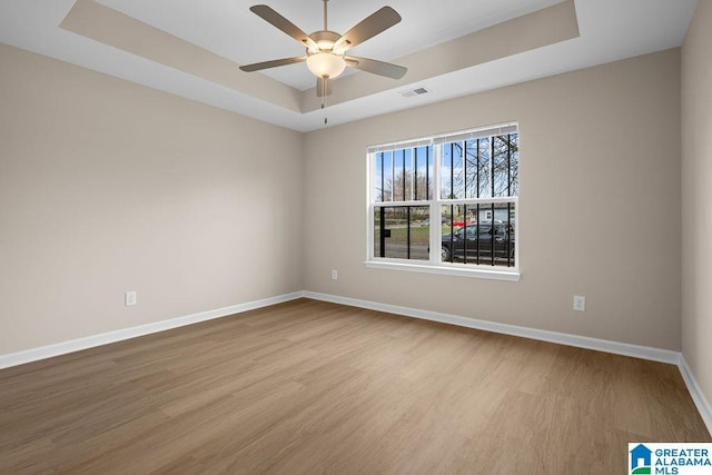 spare room with a ceiling fan, visible vents, baseboards, light wood finished floors, and a raised ceiling