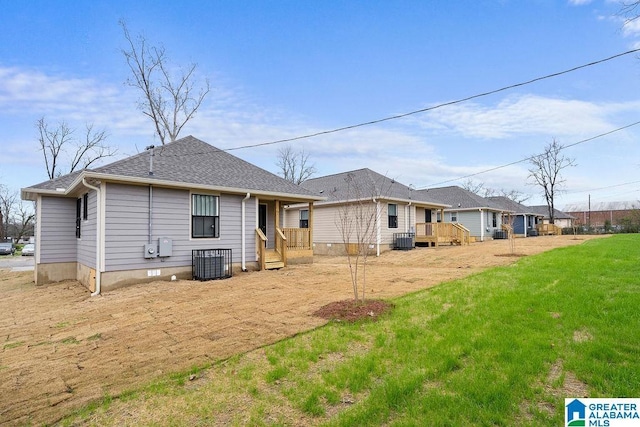 rear view of property featuring roof with shingles, a lawn, and central AC unit