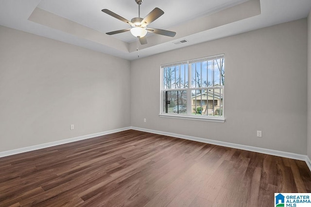 unfurnished room with a tray ceiling, wood finished floors, visible vents, and baseboards